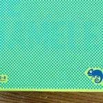 Bìa hộp game cờ bàn The Chameleon với hình ảnh tắc kè hoa và các từ khóa liên quan đến suy luận xã hội.